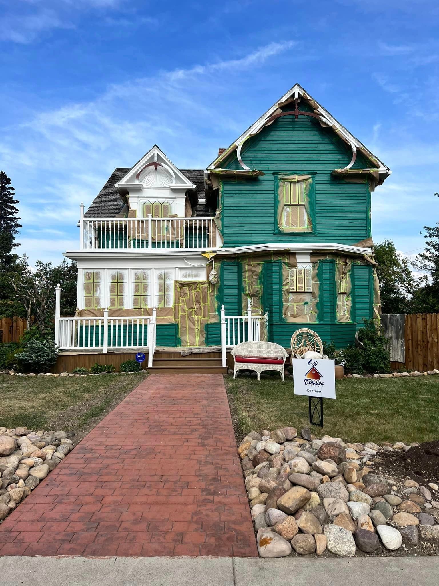 A green and white house with a brick walkway leading to it.