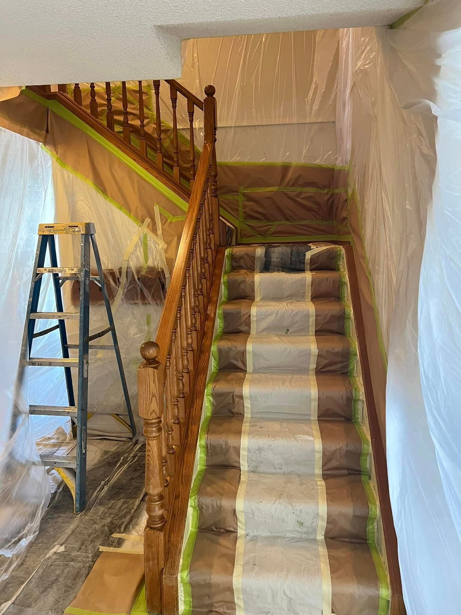 A staircase is being painted in a room with a ladder.