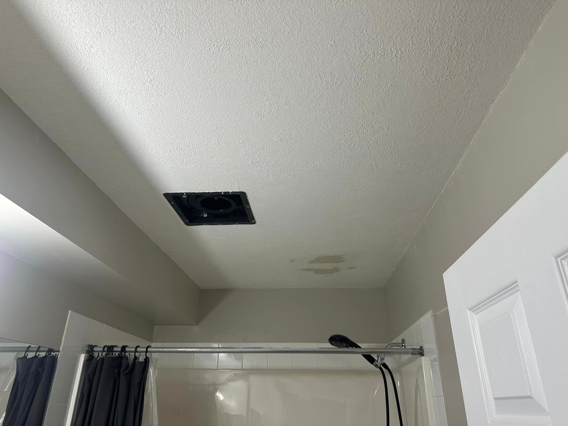A bathroom with a shower and a fan on the ceiling.