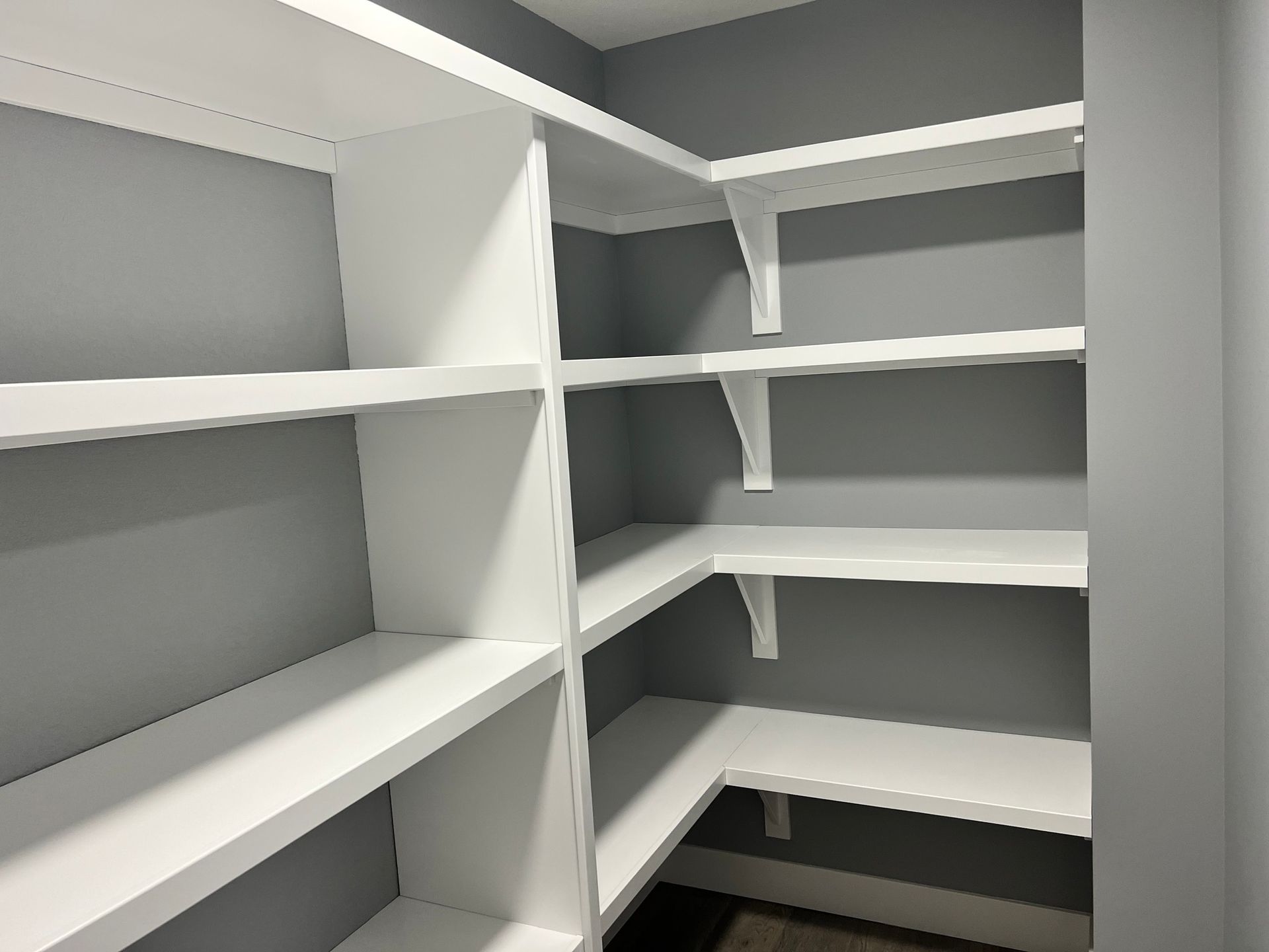 A walk in closet with white shelves and gray walls