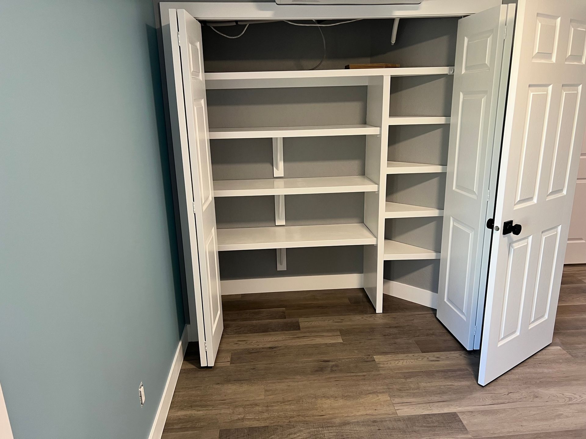 A closet with shelves and doors open in a room.