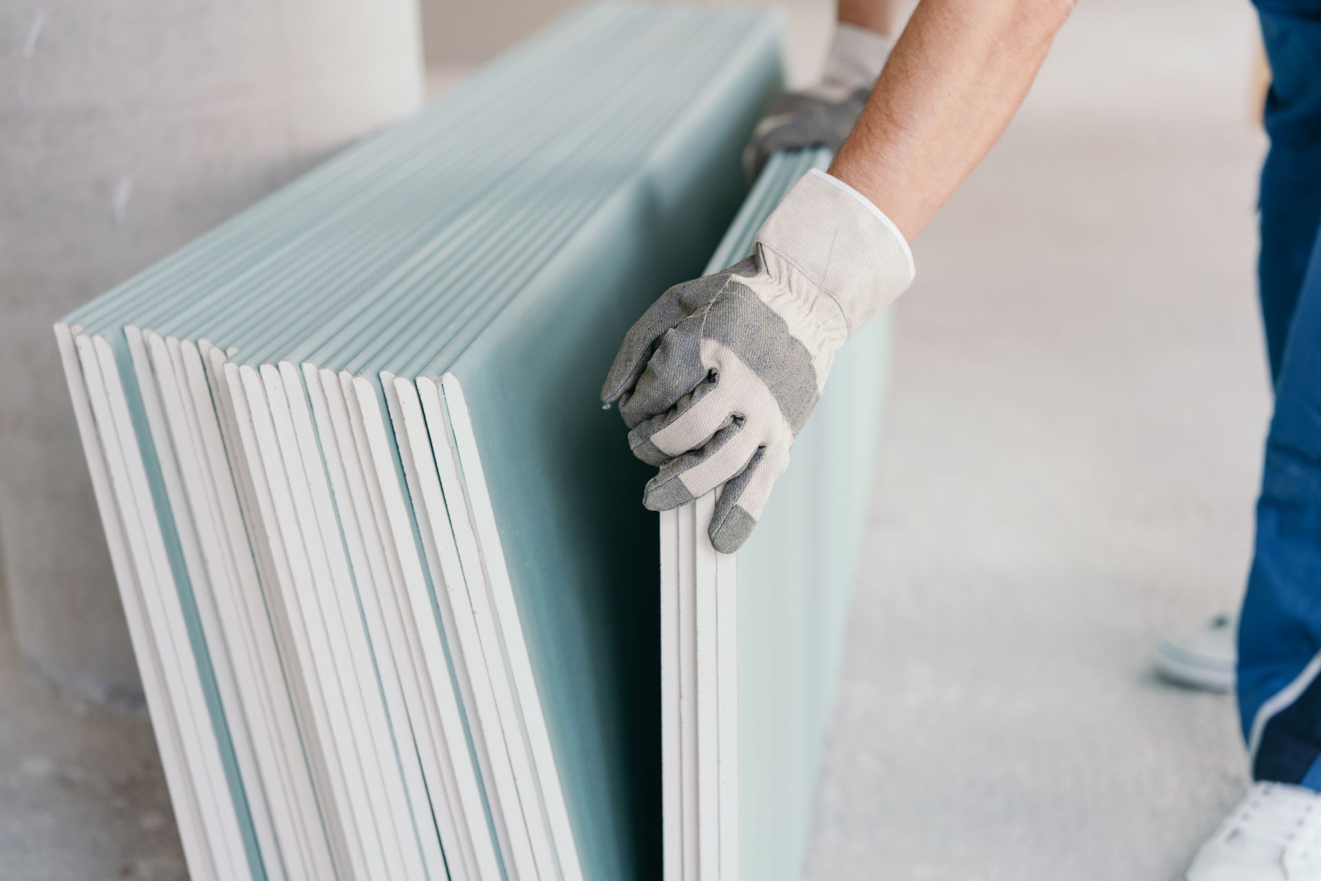 A person wearing gloves is holding a stack of drywall.
