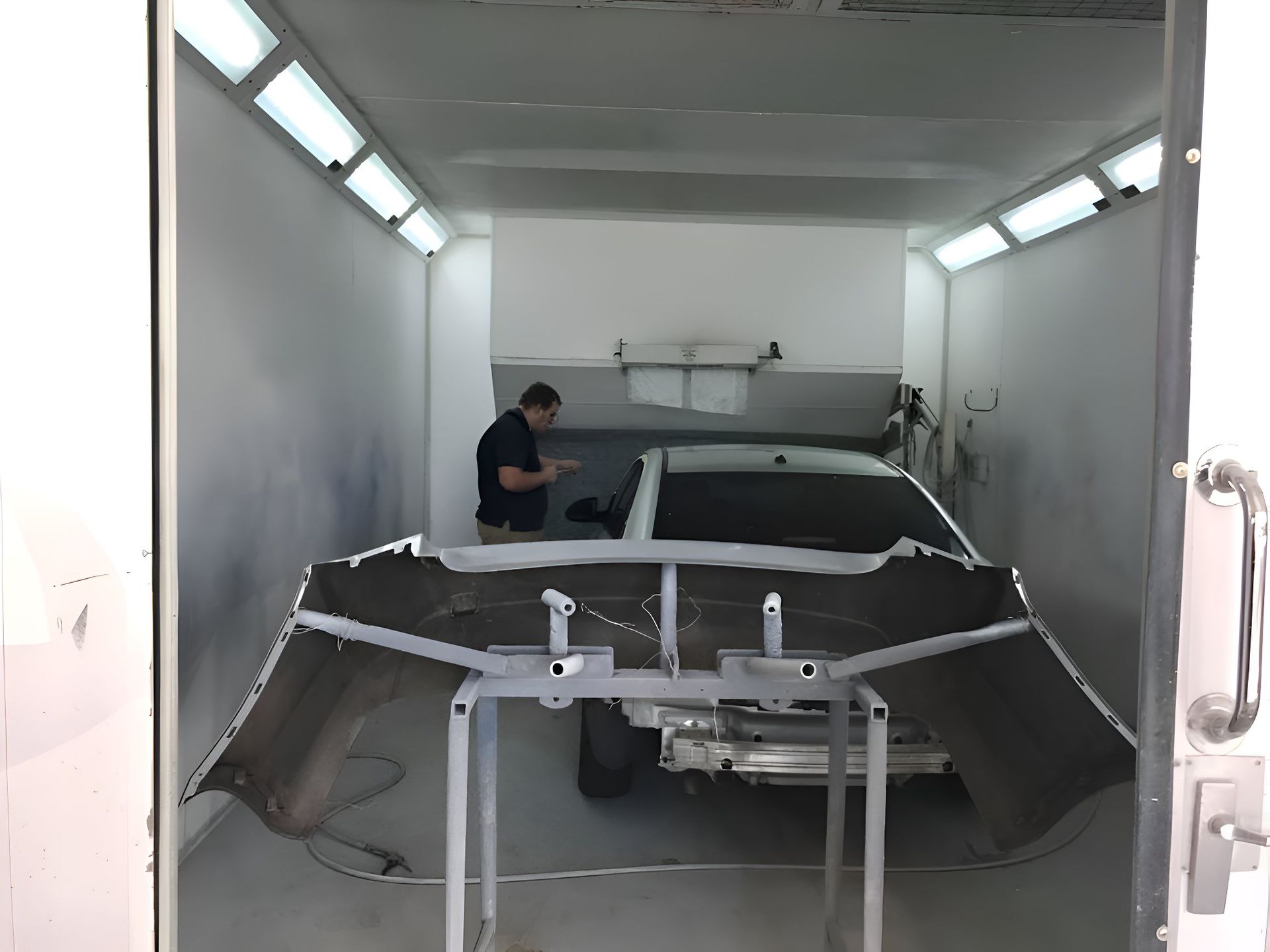 A Man Is Working On A Car In A Paint Booth — P & V Panel Works In Alice Springs, NT