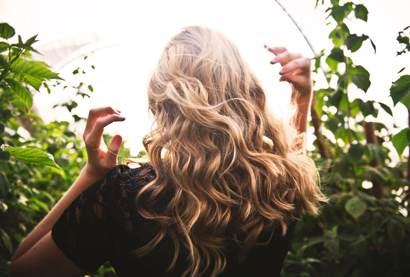 A woman with long blonde hair is standing in a greenhouse.