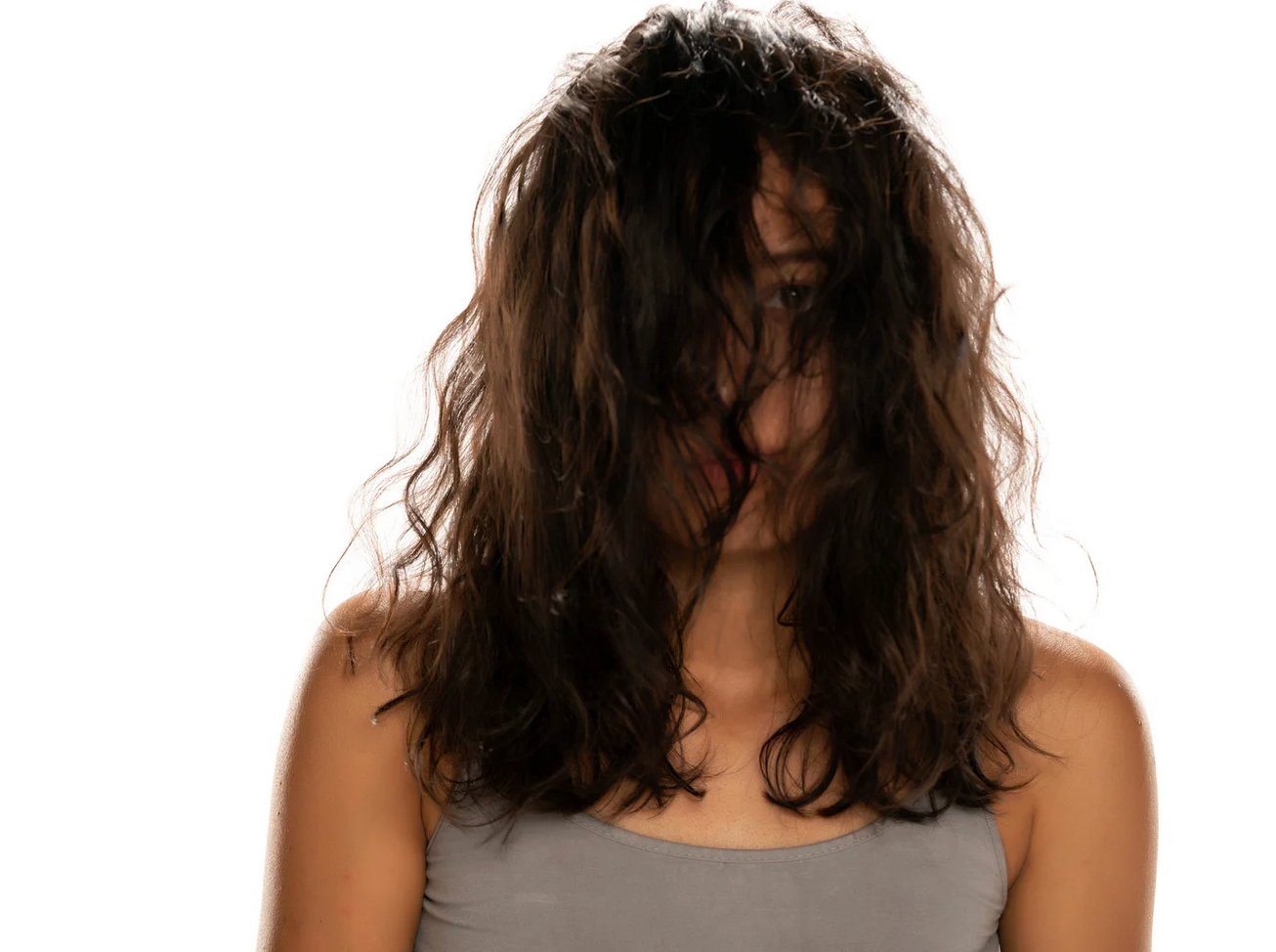 A woman with messy hair is covering her face with her hair.