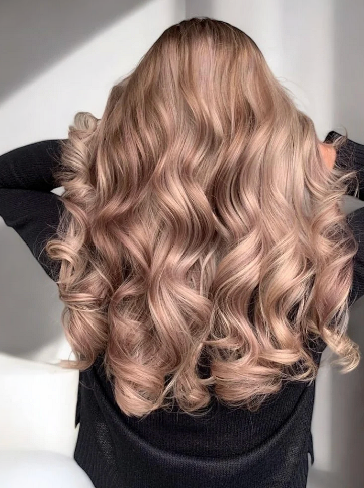A woman with long wavy blonde hair is wearing a black sweater.