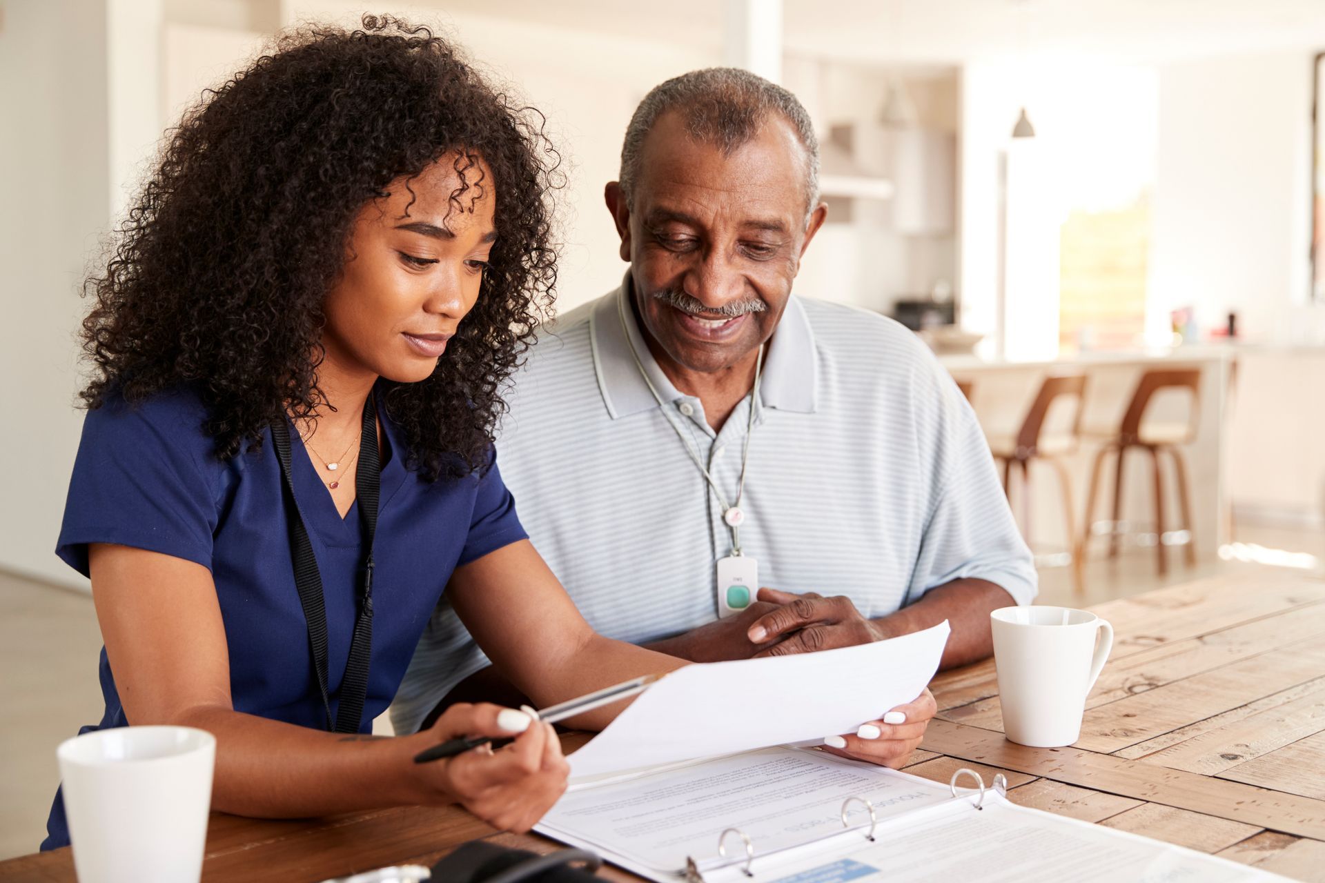 A nurse and an elderly man are sitting at a table looking at a binder.