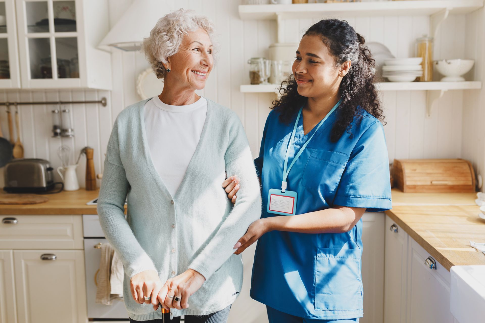 A nurse is helping an elderly woman walk in a kitchen.