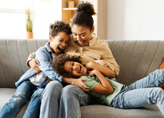 A woman and two children are sitting on a couch hugging each other.