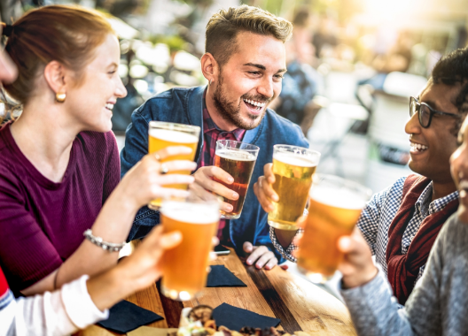 A group of people are sitting at a table toasting with beer.
