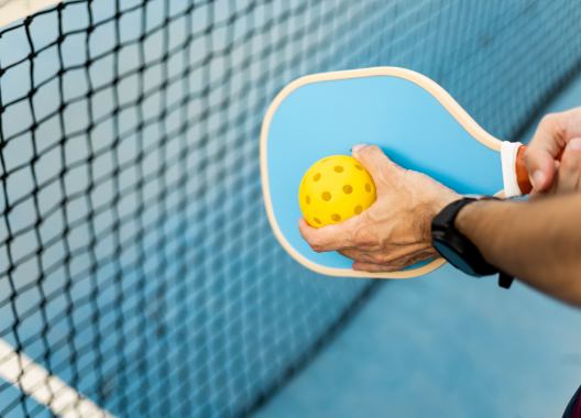 A person is holding a blue paddle and a yellow ball