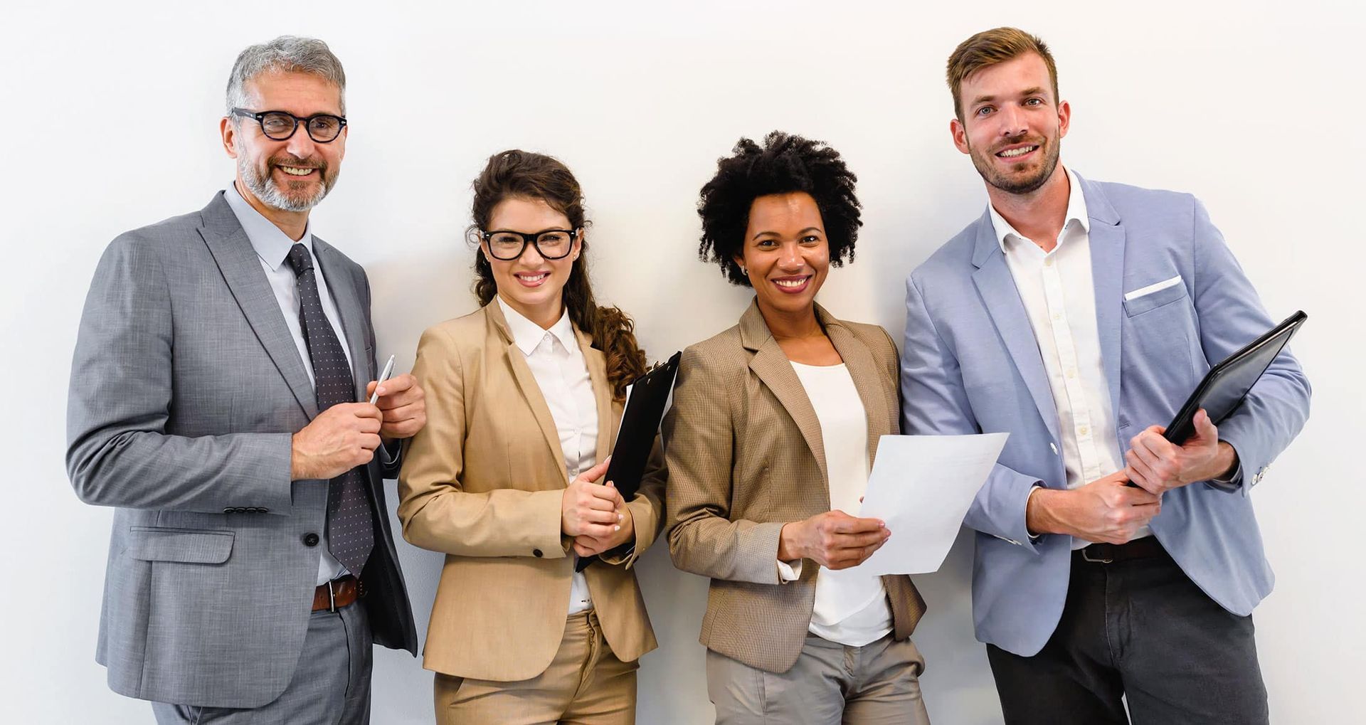 Four professionals in business attire holding documents and smiling against a white background