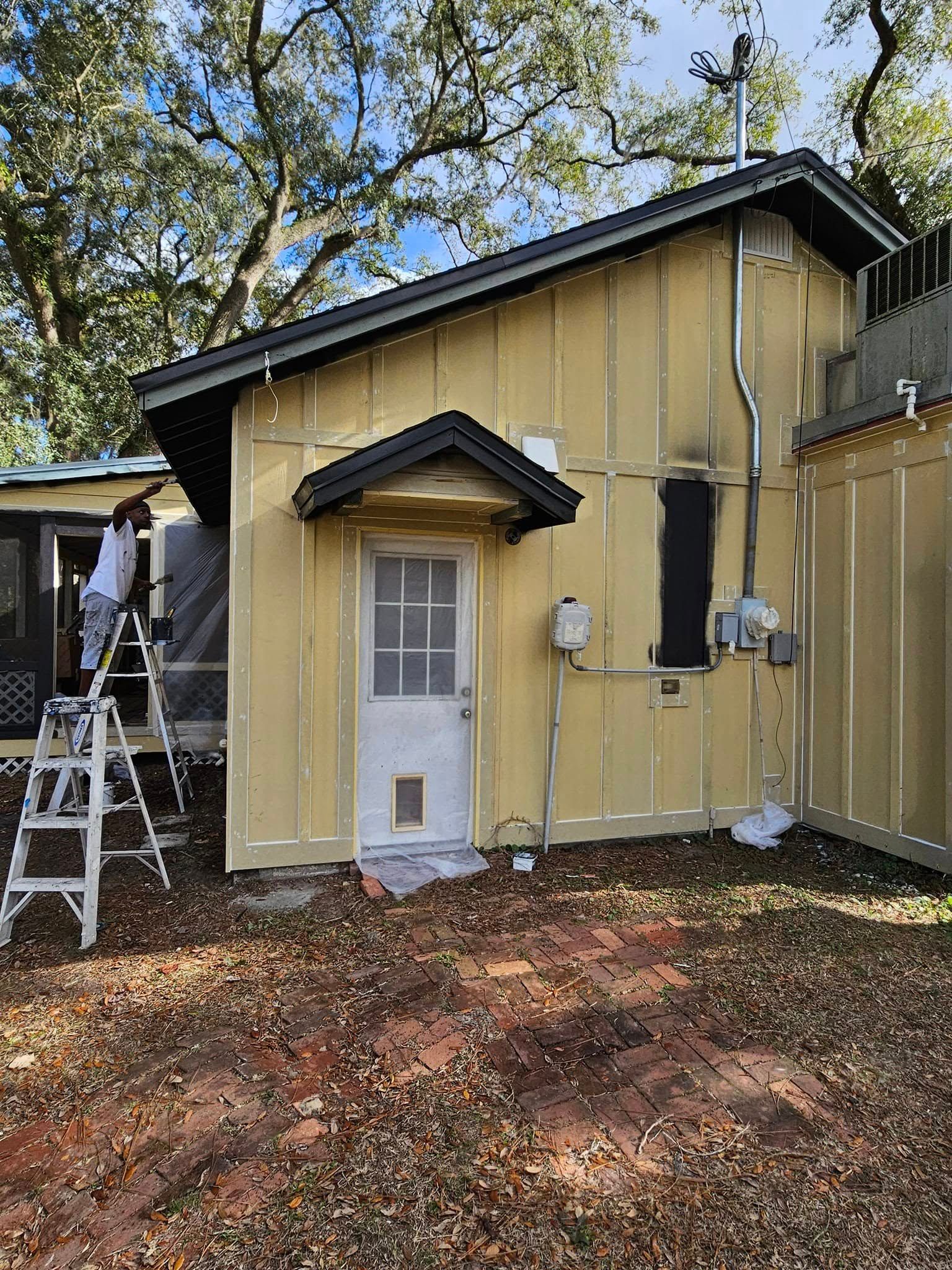 Person painting a yellow building with a black roof and door awning