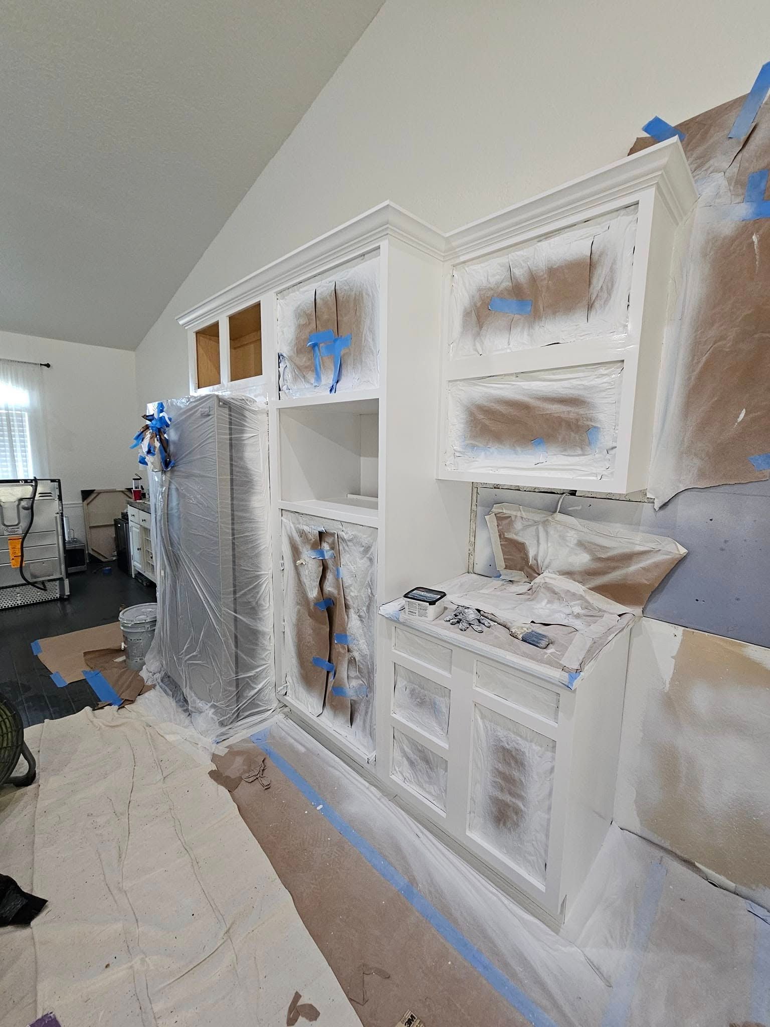 Kitchen cabinets being painted white with blue tape and drop cloths