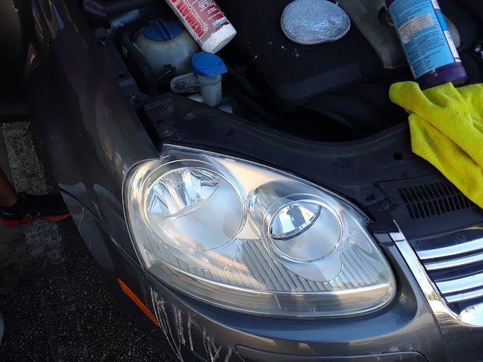 The headlight of a car is being cleaned with a yellow cloth
