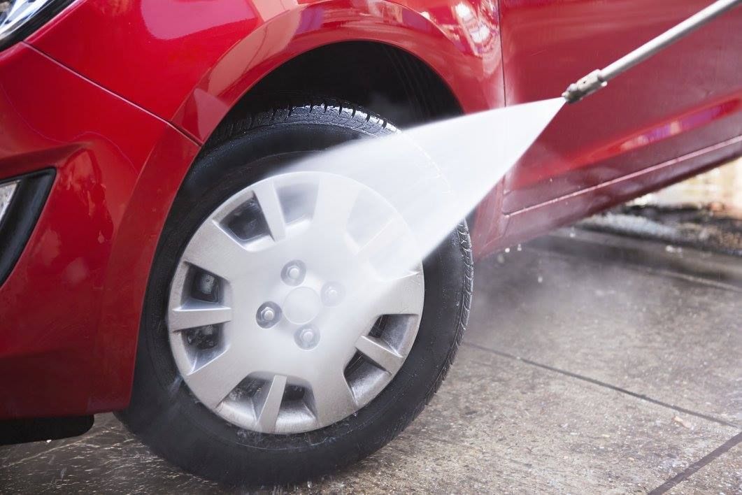 A person is washing a red car with a high pressure washer.