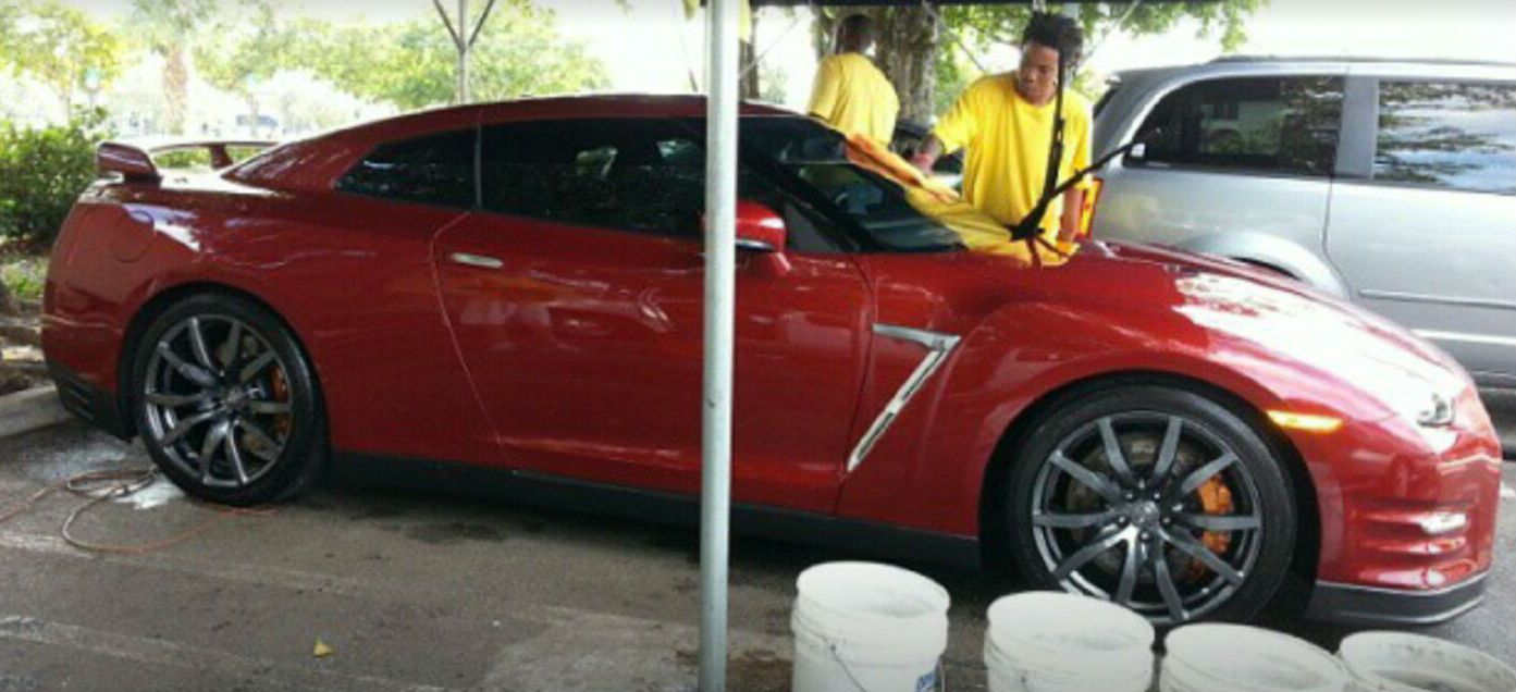 A red sports car is being cleaned by two men under a canopy.