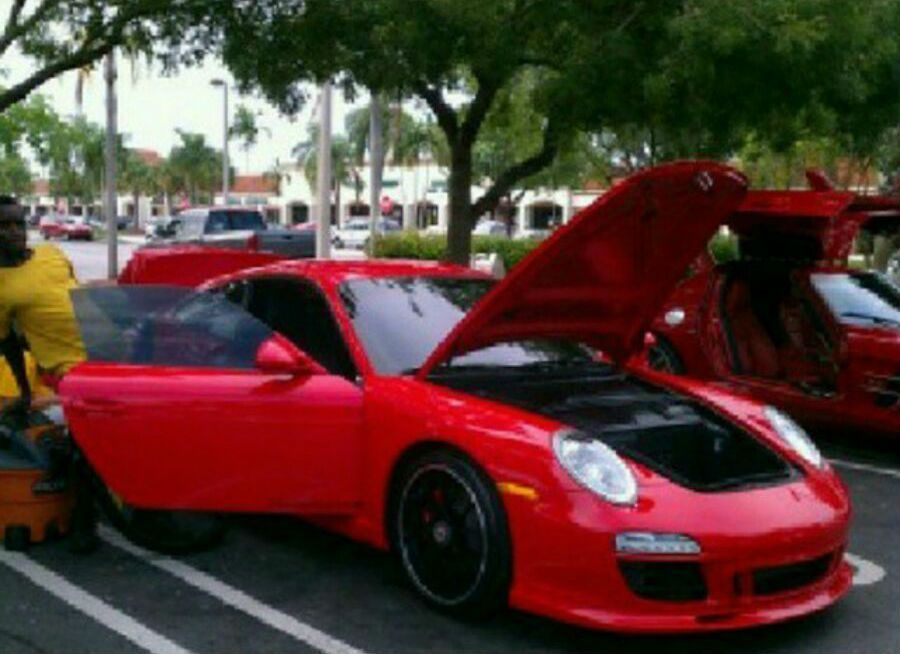 A man is standing next to a red sports car with the hood up