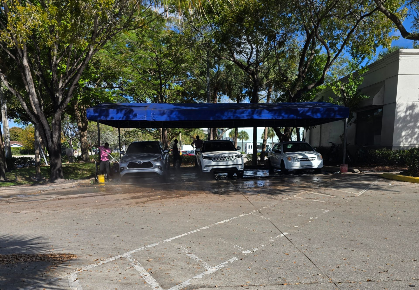 Man in yellow shirt by a blue Bentley sedan, outdoors.