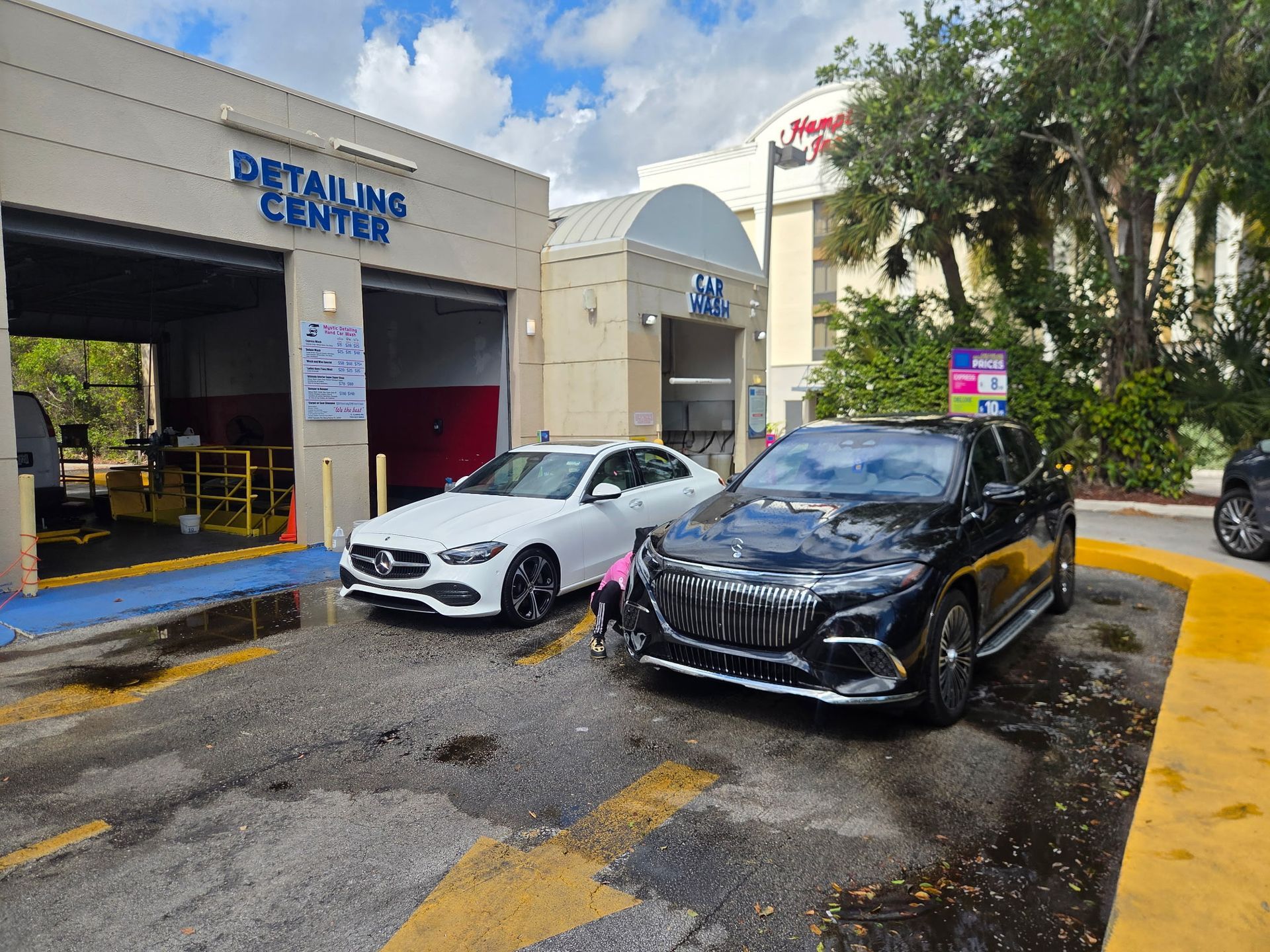 A person in yellow shirt and black shorts washing a bright yellow Porsche GT2 at a gas station.