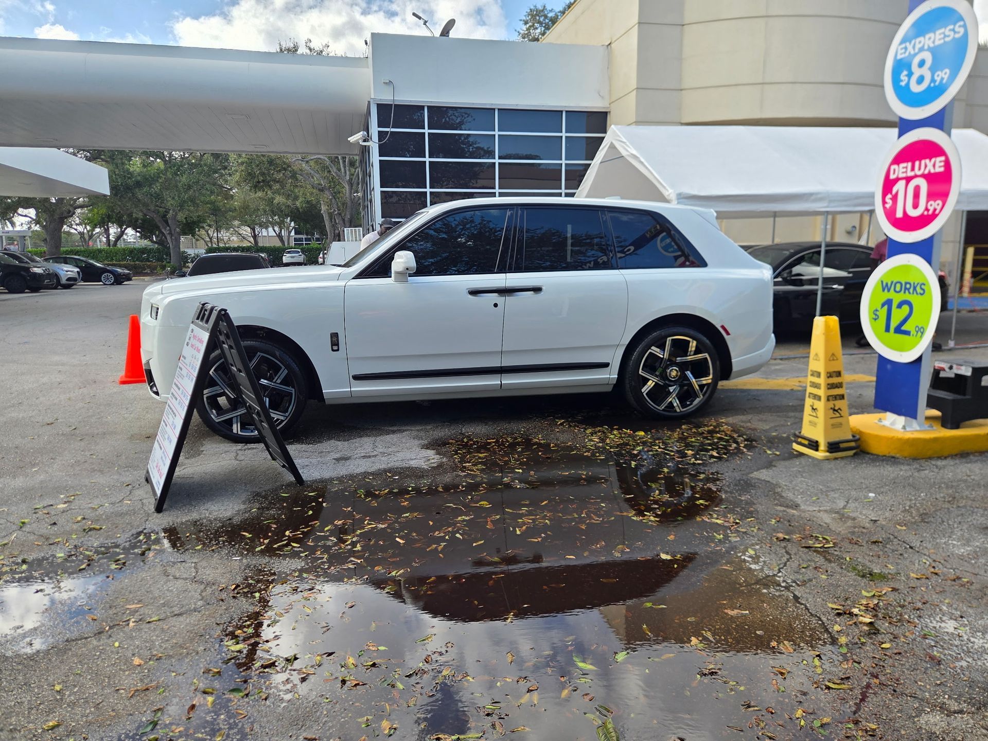 Two black Porsche sports cars with open hoods at a car wash. Workers are cleaning the vehicles.