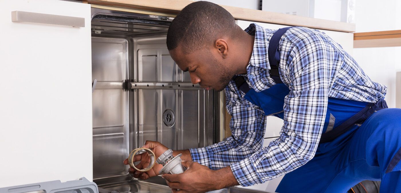 A person in work clothes repairing a dishwasher.