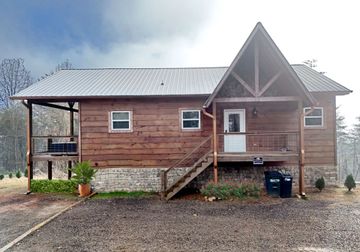 Rustic wooden cabin with a front porch and gabled roof on a gravel driveway