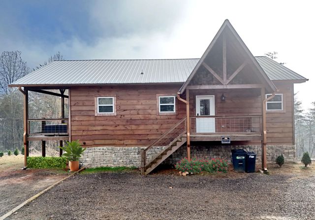 Rustic wooden cabin with a front porch and gabled roof on a gravel driveway