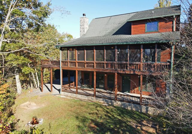 Wooden cabin with screened porch and stone foundation, surrounded by trees on a sunny day