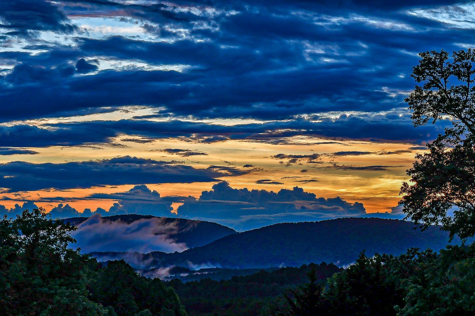 Five people stand on a cabin deck at sunset, overlooking mountains and autumn trees.