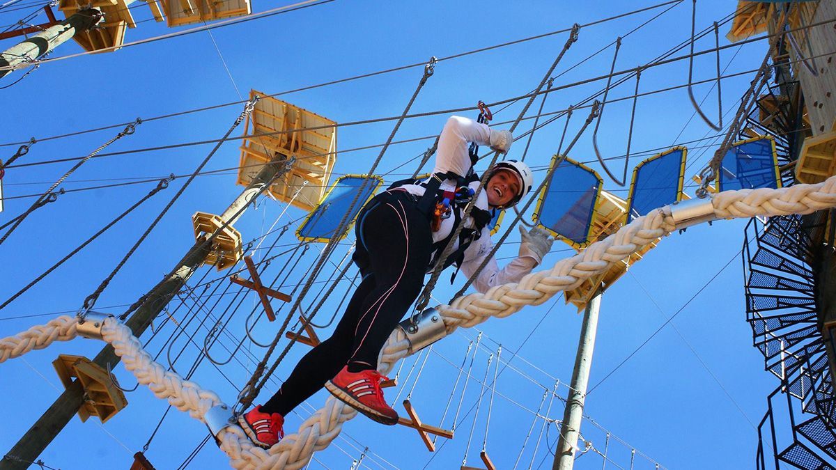Person climbing a rope adventure course among suspended platforms against a blue sky
