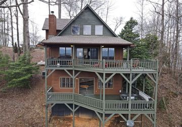 Rustic multi-level cabin with green wraparound porches on a wooded hillside
