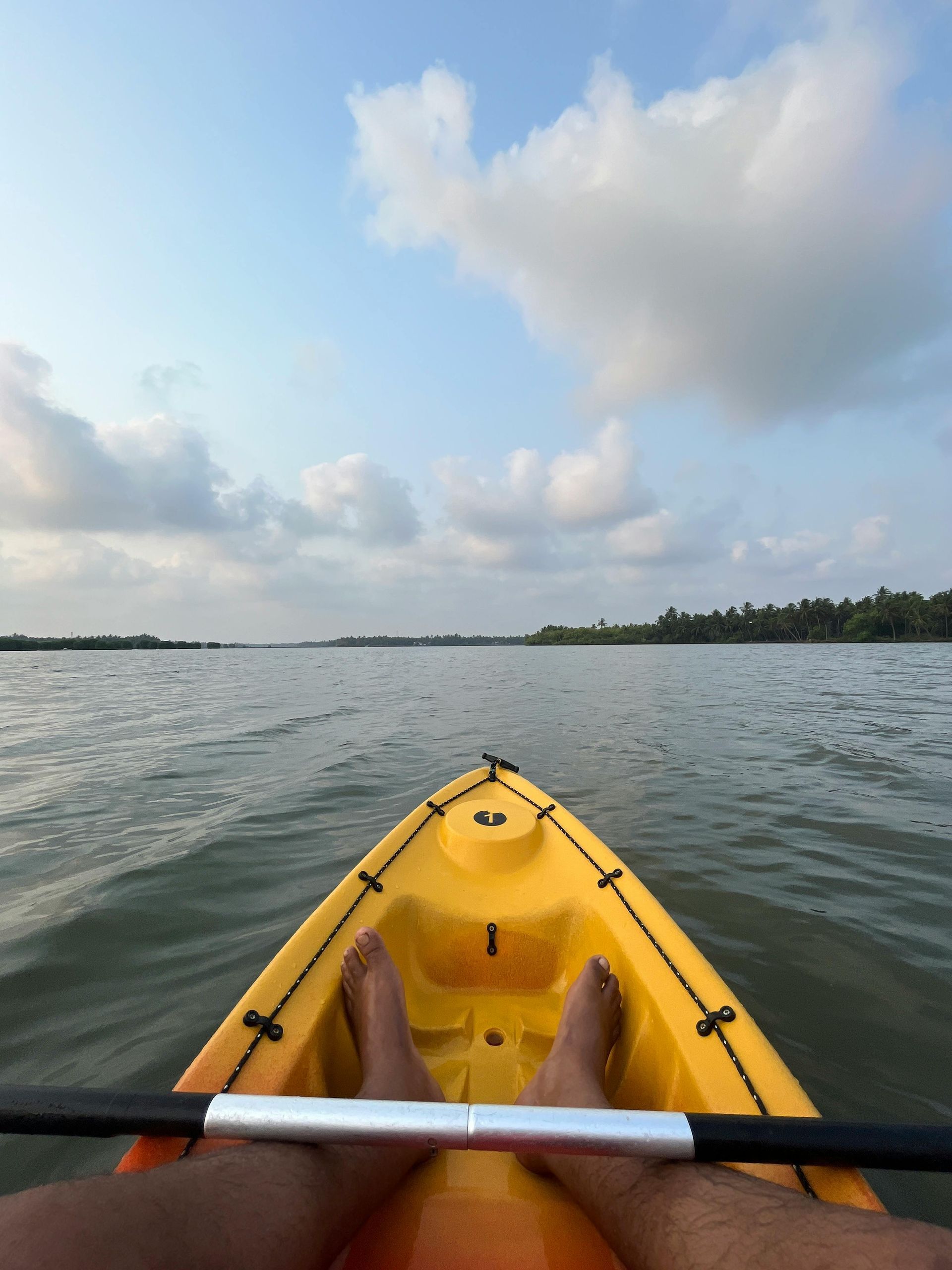 View from a yellow kayak on calm water at sunset, with feet visible and a cloudy sky overhead