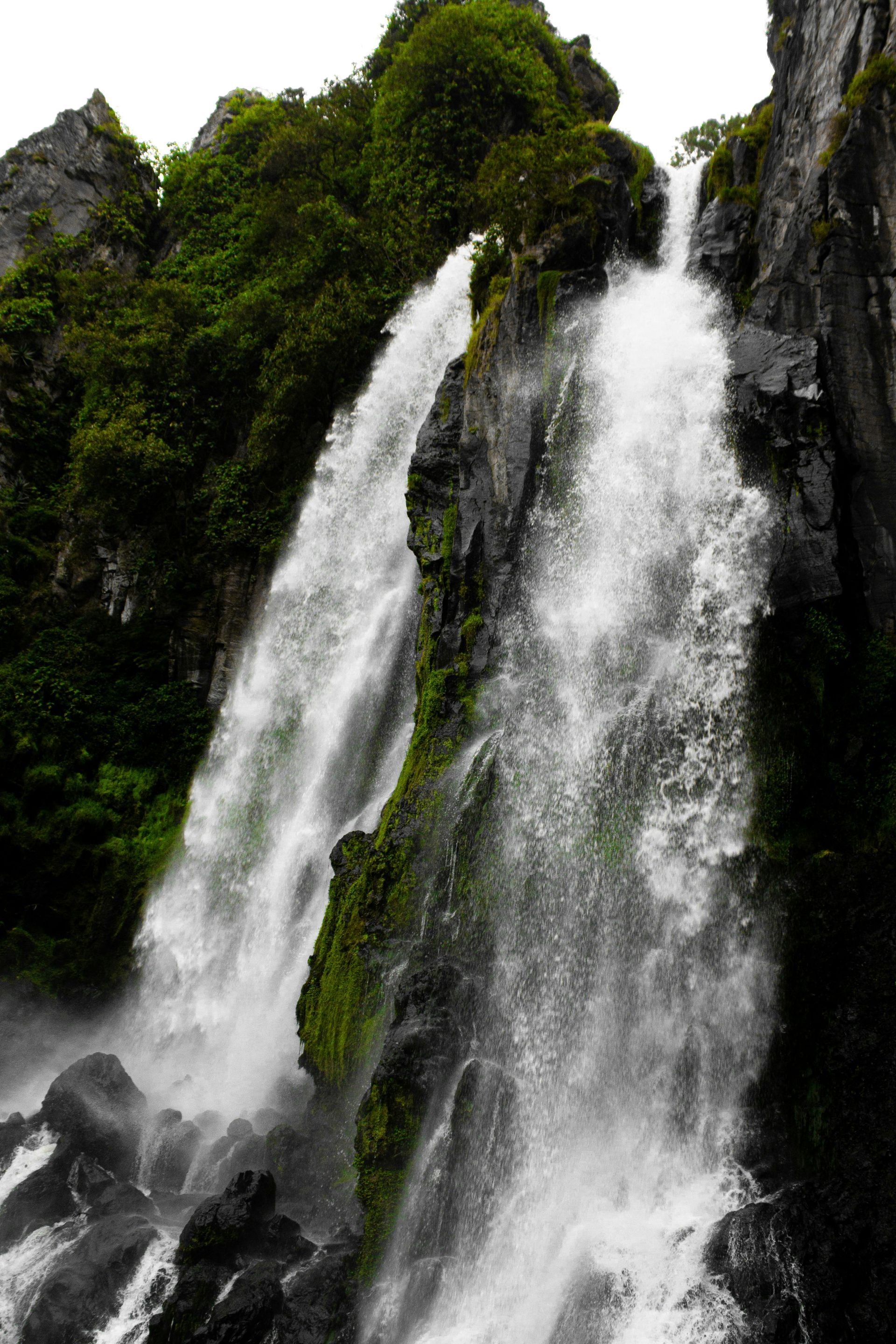 Tall white waterfall cascading over dark rocks with green moss and foliage