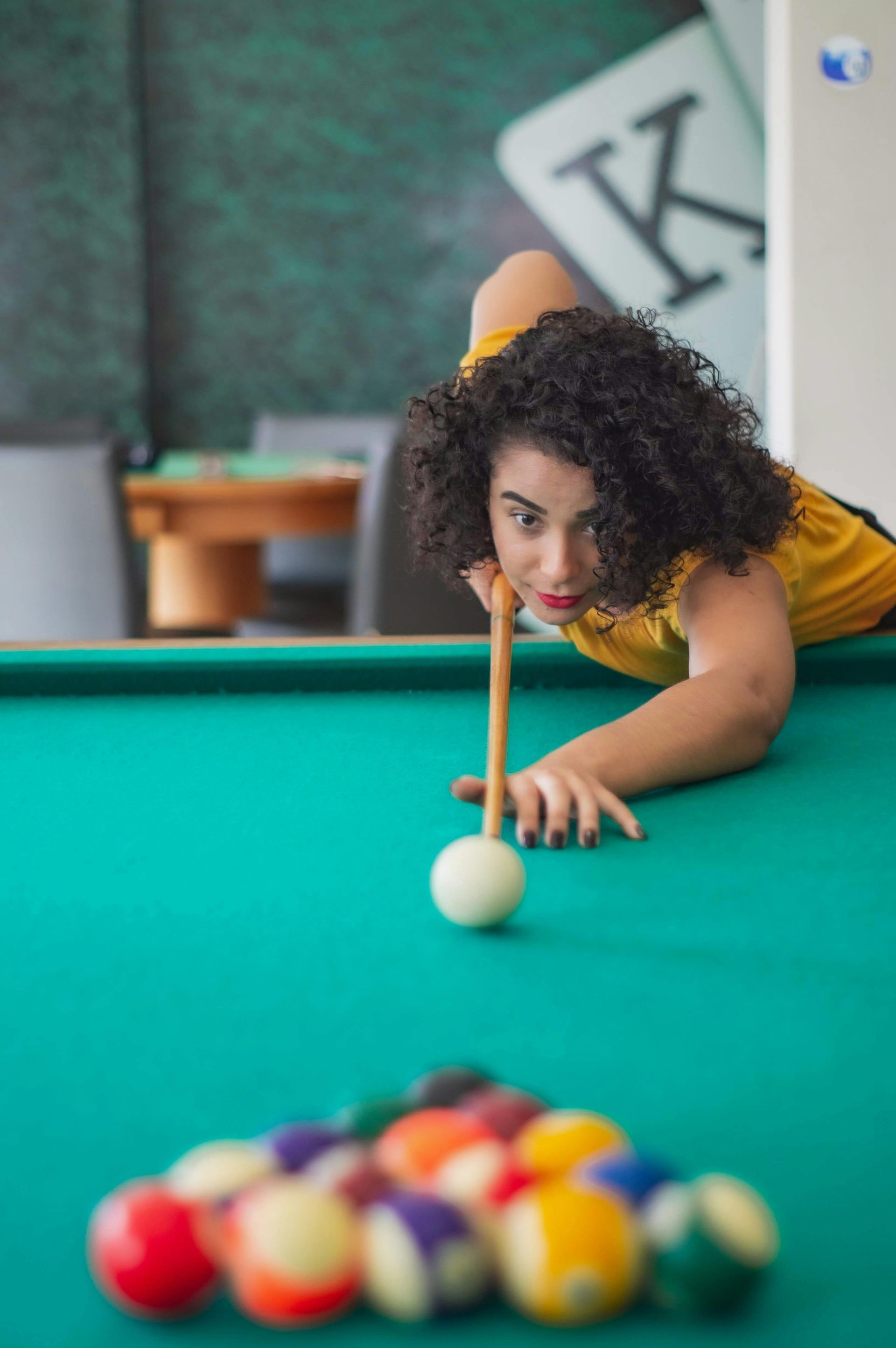 Person lining up a pool shot over a teal billiards table, with a rack of balls in the foreground.