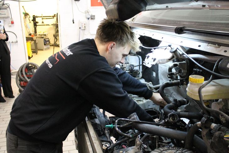 Mekaniker arbejder på en bilmotor under motorhjelmen i en garage.