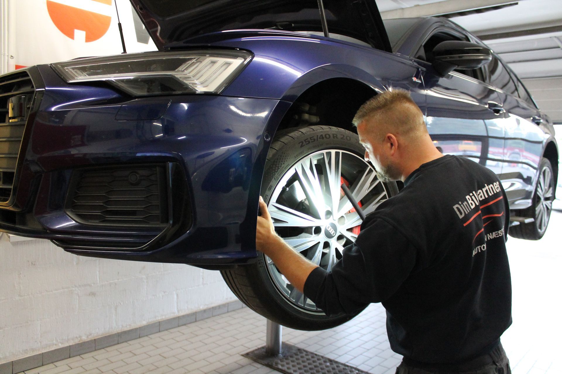 Mekaniker inspicerer bildæk i et værksted. Blå bil på en lift.