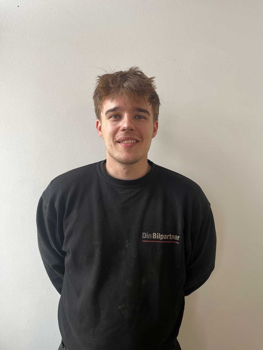 Mand i sort sweatshirt står op ad en hvid væg med hænderne bag ryggen.