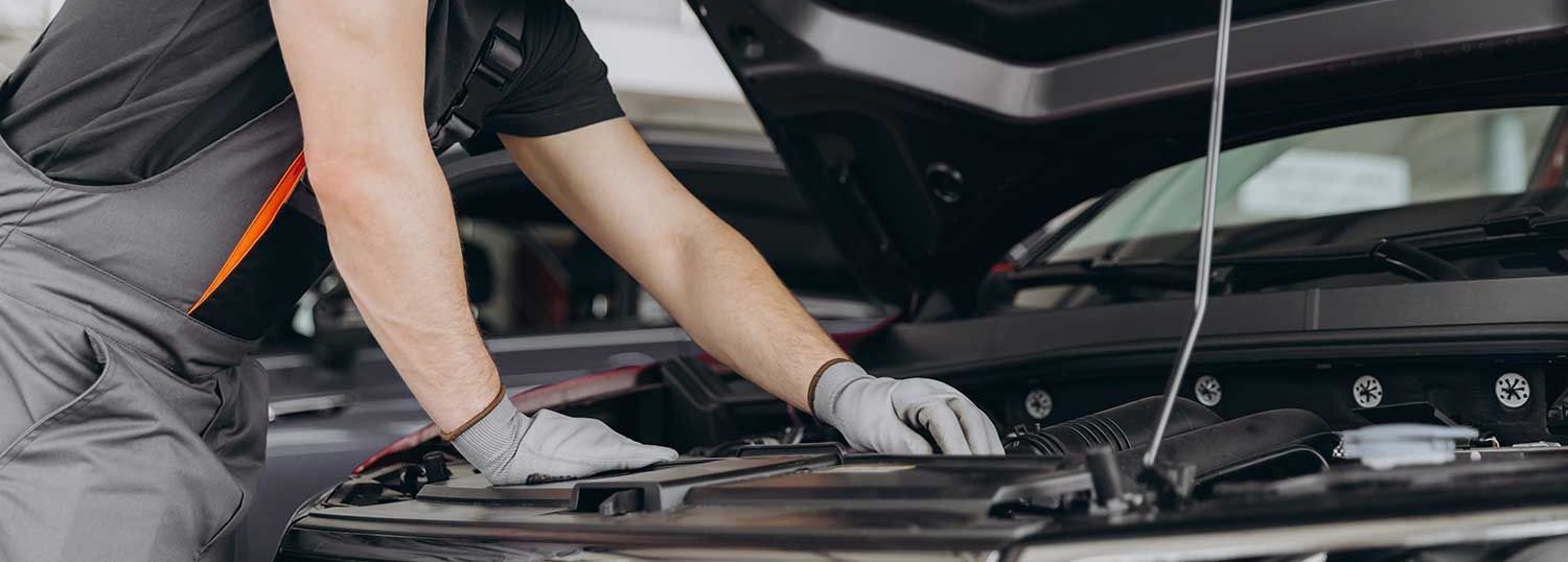 Mekaniker arbejder på en bilmotor, iført handsker, i en garage.