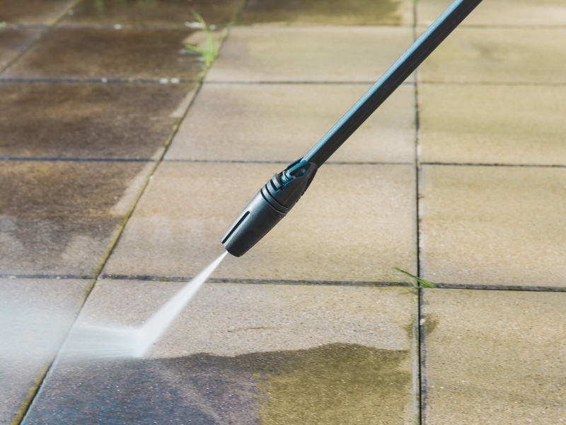 A person is using a high pressure washer to clean a paved floor.