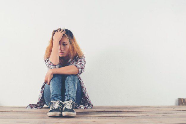 A woman is sitting on a wooden floor with her head in her hands.
