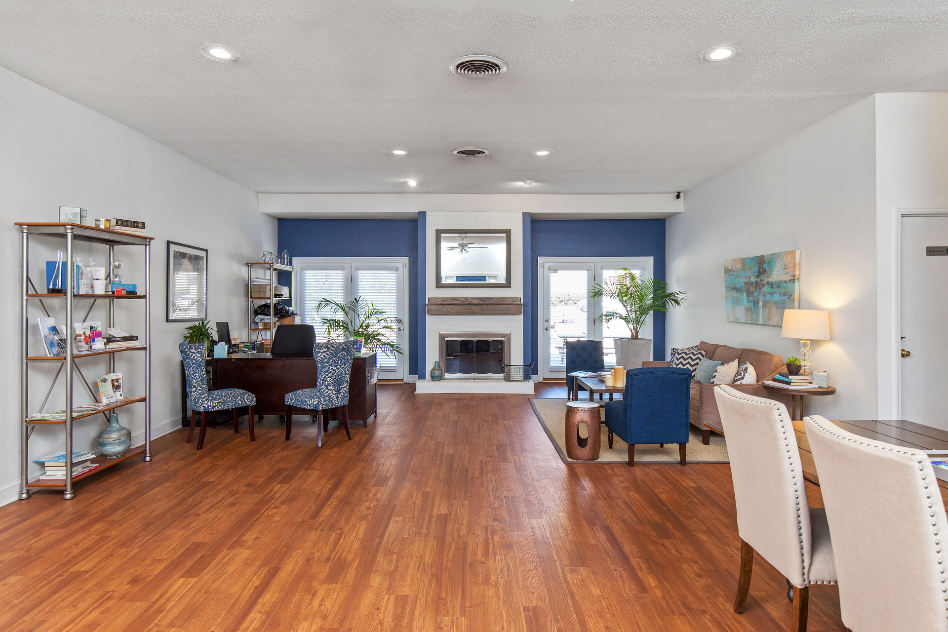 A spacious living area with hardwood floors, a central fireplace, a desk, a seating area, and dining chairs.