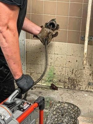 A man is using a machine to clean a drain in a bathroom.