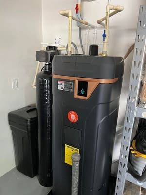 A water softener is sitting in a room next to a trash can.