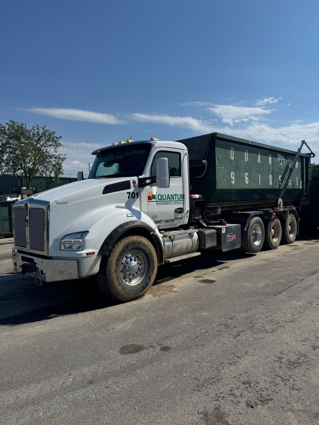 White dump truck with green trailer parked outdoors on a sunny day