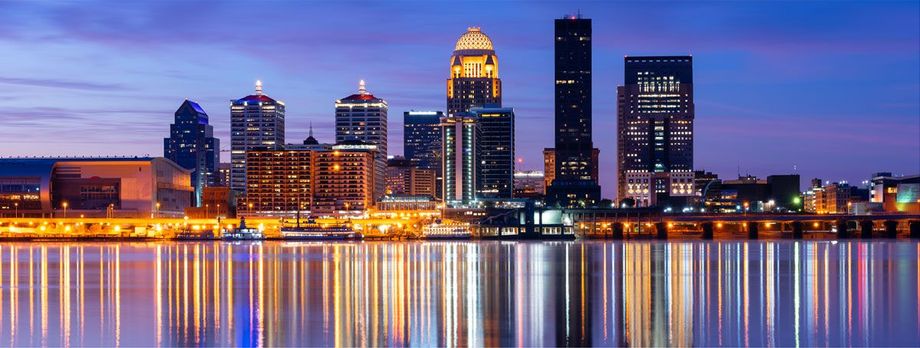 City skyline at dusk with lit buildings reflected in calm water