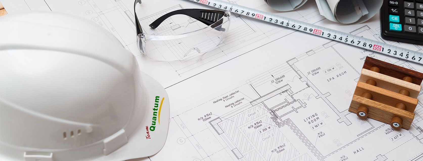 White hard hat on architectural blueprints beside a pencil, calculator, and small wood blocks on a desk