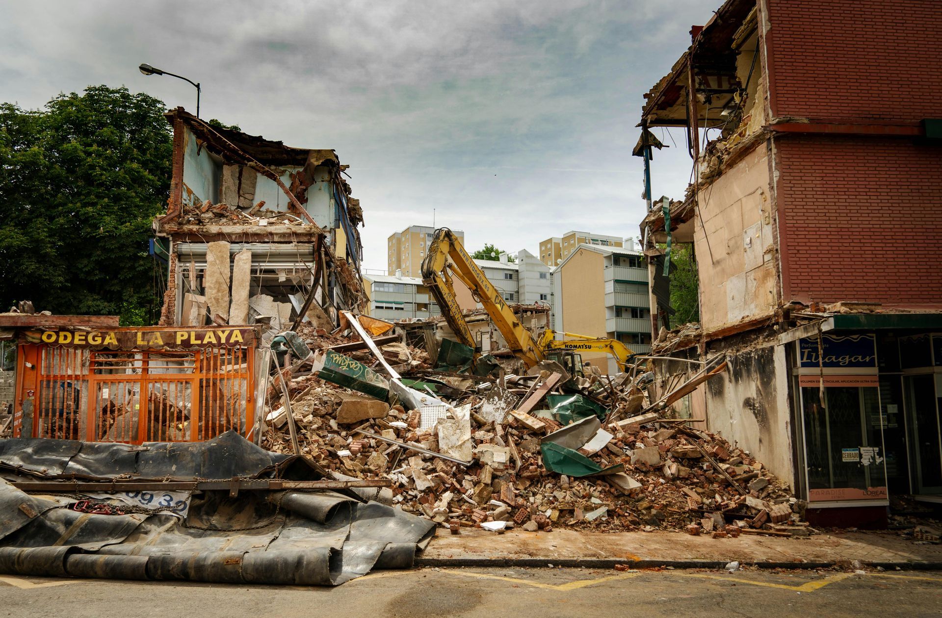 Collapsed buildings and rubble after demolition, with an excavator amid debris on a city street.