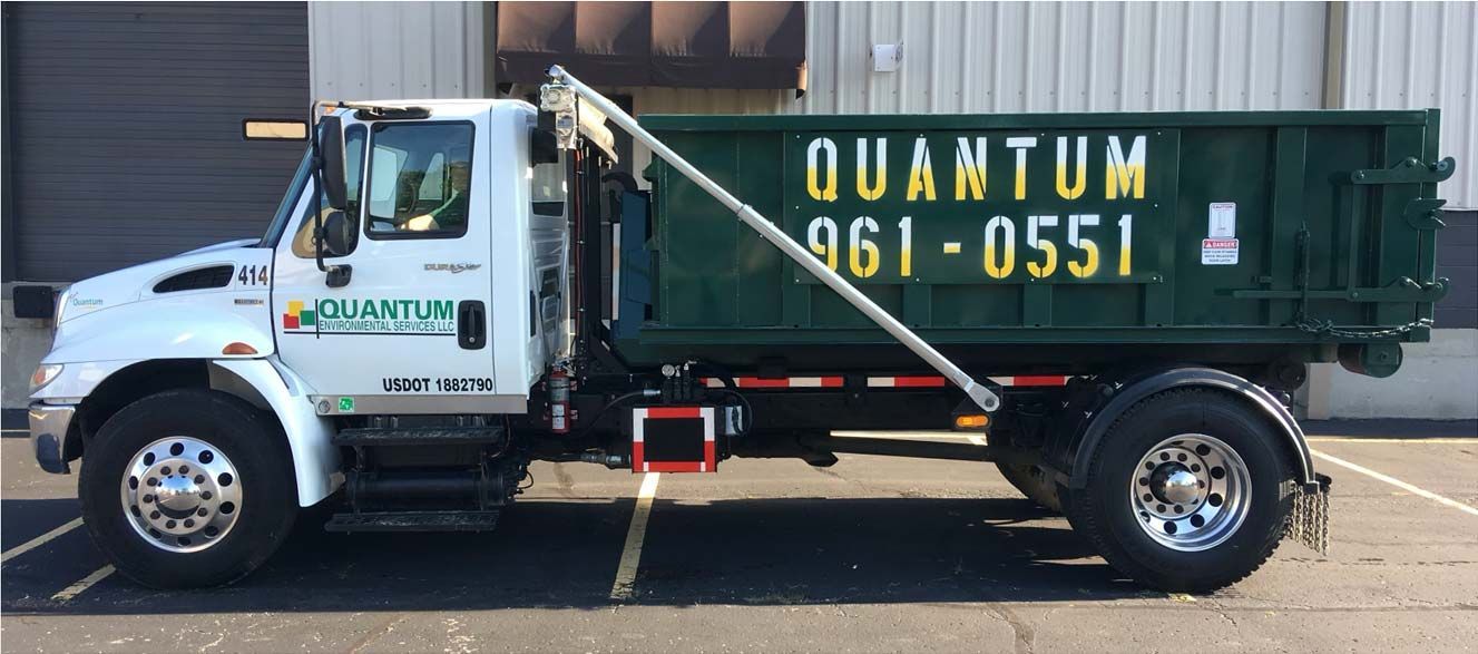 Green dump truck with yellow lettering parked in a lot, side view
