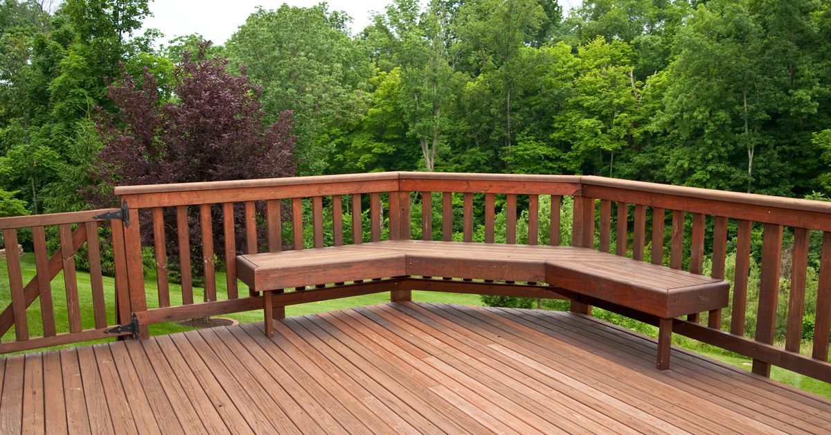 A wooden deck with a bench and trees in the background
